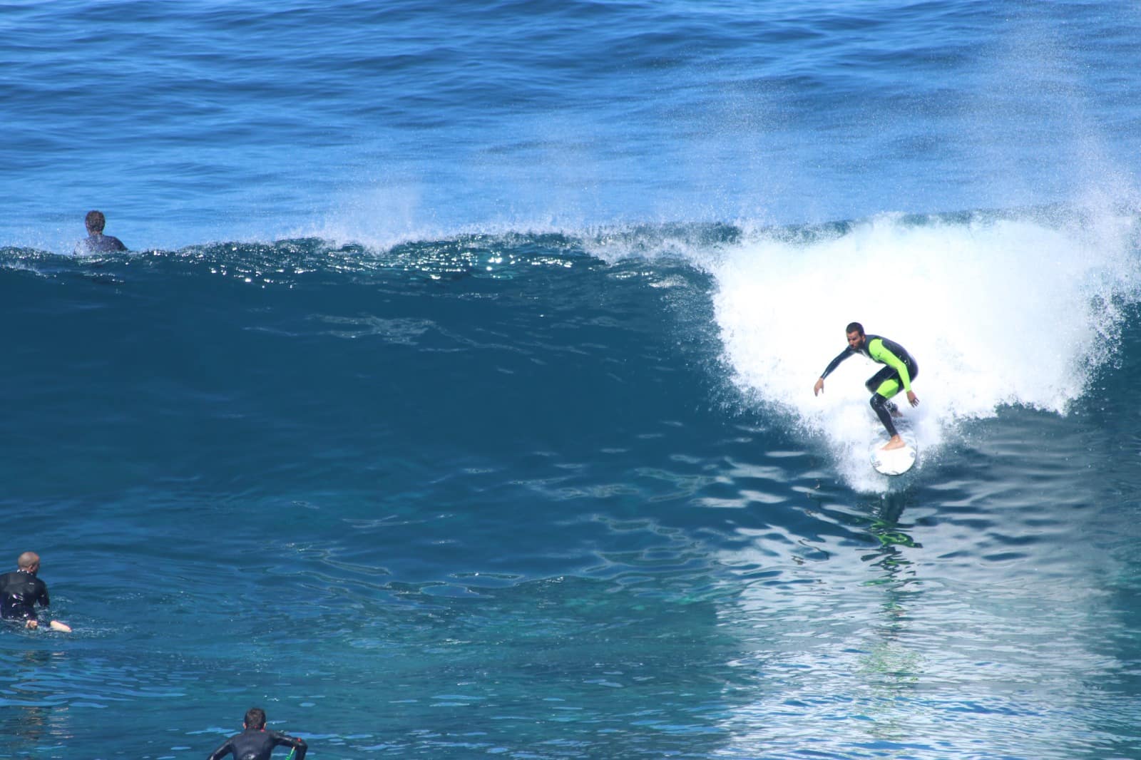 Surfista de fato escuro e verde a surfar uma onda de água azul.